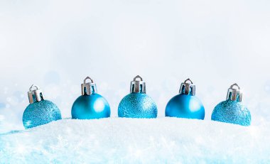Beş mavi noel süsü karda bir sırada duruyor