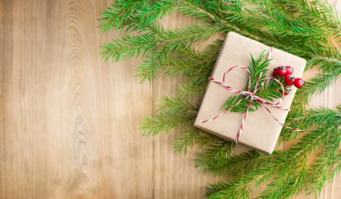 Ahşap bir arka planda köknar dalları ve böğürtlenlerle süslenmiş Noel hediyesi