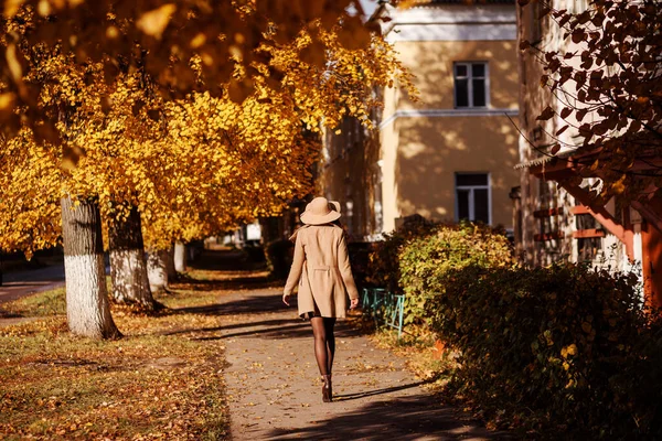 Stylish woman in beige coat and is walking away down the street in autumn. — Stock Photo, Image