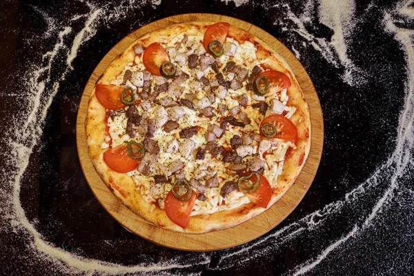 Top view of meat pizza with mozzarella cheese, jalapenos, tomatoes on dark table