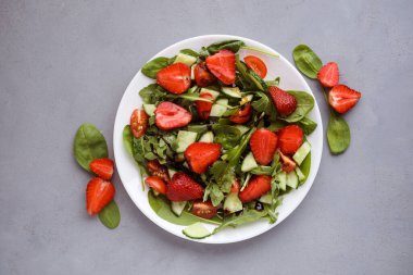 Çilek, roka, ıspanak, salatalık ve balzamik sostan yapılmış lezzetli bir salata. Gri arkaplan.