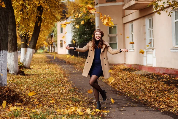 Веселая женщина веселится, осенью выбрасывает листья на улицу. — стоковое фото