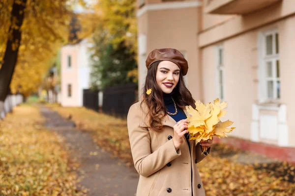 Stylische Frau mit brauner Baskenmütze und beigem Mantel verbringt im Herbst Zeit im Freien. — Stockfoto