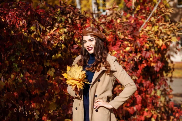 Smiling woman is spending time outdoors in autumn. Red leaves hedge background. — Stock Photo, Image