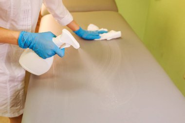 Güzellik uzmanı, doktor müşteri kanepesini dezenfektanla temizler. İşyeri hijyeni.