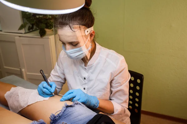 A szőrtelenítő specialista elektro epilációt végez. Maszkot és pajzsot viselő nő. — Stock Fotó