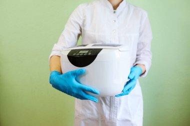 Doctor, beautician or dentist holds ultrasonic sterilizer in her hands in gloves clipart