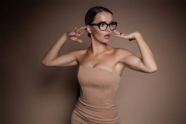 Hermosa mujer de negocios en un vestido de negocios y gafas sobre un fondo marrón en el estudio —  Fotos de Stock