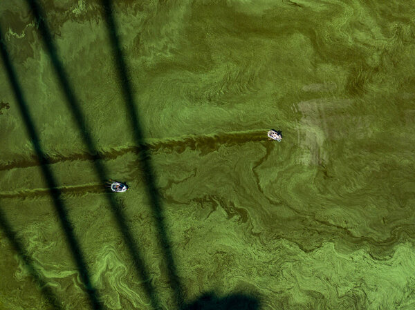 Aerial drone view. Two fishing boats in the shadow of the North Bridge in Kiev. Green blooming algae in the Dnieper river on a hot summer day.