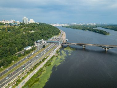 Kiev metrosunun trenleri Dinyeper nehri üzerindeki köprüye gidiyor. Güneşli bir yaz günü. Hava aracı görünümü.