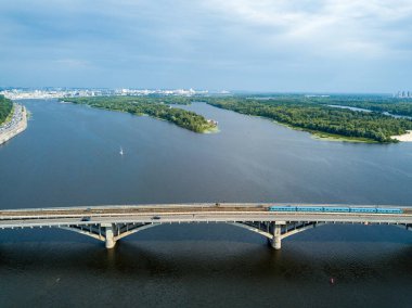 Kiev metrosunun trenleri Dinyeper nehri üzerindeki köprüye gidiyor. Güneşli bir yaz günü. Hava aracı görünümü.