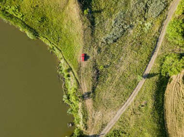 Hava aracı görüntüsü. Göl kenarındaki yeşil çayır üzerinde kırmızı araba..
