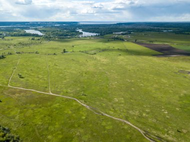 Hava aracı görüntüsü. Yeşil bir çayırda kirli bir yol.