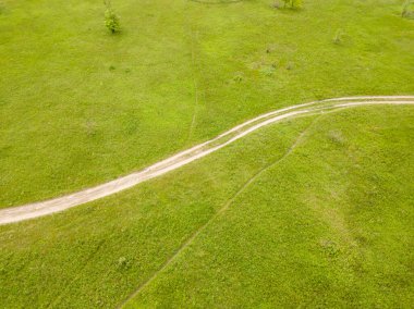 Hava aracı görüntüsü. Yeşil bir çayırda kirli bir yol.