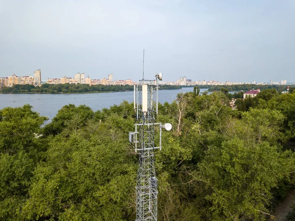 Cellular relay tower against the background of the city and the river. Aerial drone view.