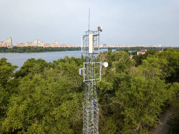 Cellular relay tower against the background of the city and the river. Aerial drone view.