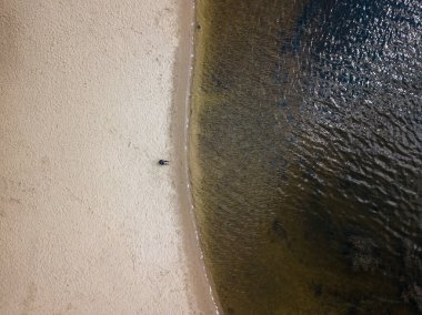 Hava aracı görüntüsü. Nehrin kıyısında kumların üzerinde oturan kadın.