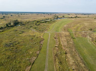 Yeşil çayırların arasındaki toprak yol. Yaz güneşli bir gün. Hava aracı görünümü.