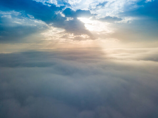 Беспилотник летит над туманом. Внизу густые туманы, солнце прорывается сквозь облака..