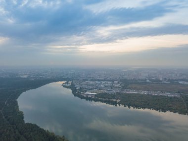 Hava aracı görüntüsü. Şehrin varoşlarındaki göl. Göl, günbatımının ışınlarında gökyüzünü yansıtır. Bulutlu.