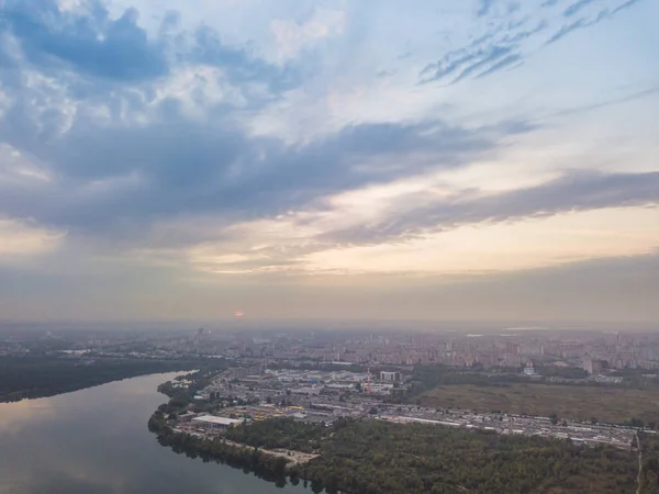 Aerial drone view. Lake on the outskirts of the city. The lake reflects the sky in the rays of the sunset. Cloudy.