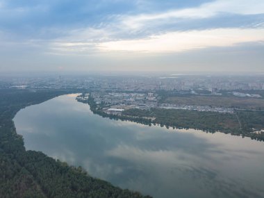 Hava aracı görüntüsü. Şehrin varoşlarındaki göl. Göl, günbatımının ışınlarında gökyüzünü yansıtır. Bulutlu.
