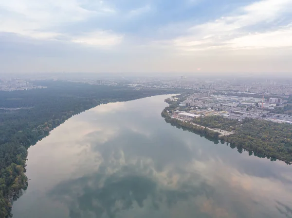 Aerial drone view. Lake on the outskirts of the city. The lake reflects the sky in the rays of the sunset. Cloudy.