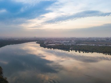 Hava aracı görüntüsü. Şehrin varoşlarındaki göl. Göl, günbatımının ışınlarında gökyüzünü yansıtır. Bulutlu.