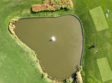 Hava aracı görüntüsü. Yeşil golf sahasında çeşmeli bir göl.