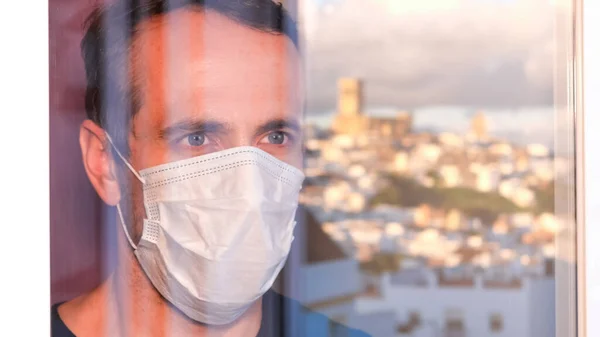 Blue-eyed man with a protective mask looking out the window. Selective focus.