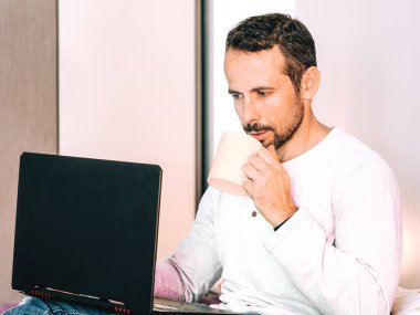 Yatak odasında bilgisayarını tamir ederken kahve içen bir adam. Evde çalışma kavramı. Seçici odak