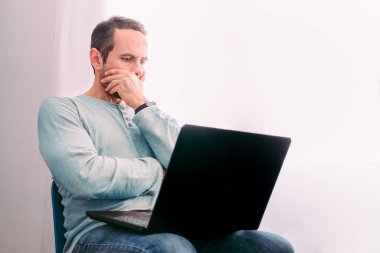 Ciddi bir adam balkonun yanındaki laptop ekranına bakıyor. Seçici odak