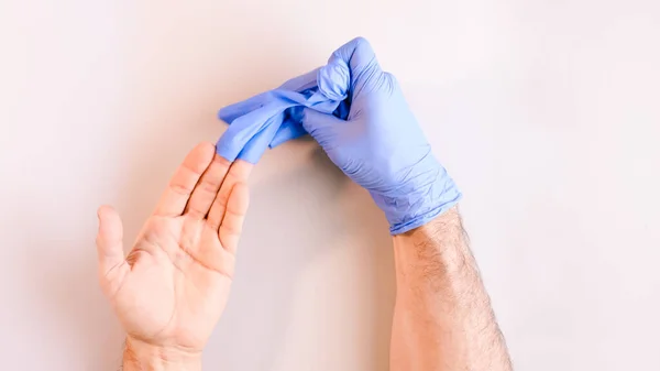 Image 4 of a sequence of images in which a man\'s hands taking off blue disposable gloves medical. Top view. Selective focus