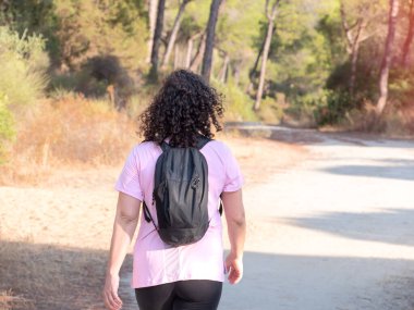 Güneşli bir günde, güzel bir doğal ortamda, huzurlu bir toprak yolda yürüyen sırt çantalı bir kadının dikiz görüntüsü..