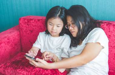 Genç Anne ve küçük kızı evde koltukta bir smartphone kullanıyorsanız