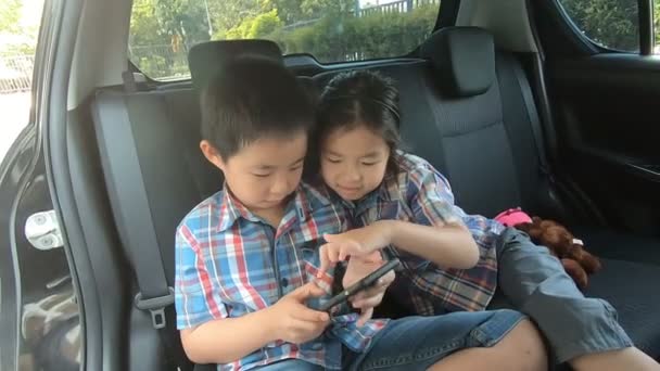 車の中でスマートフォンを保持シートベルトを着て幸せな小さな男の子の女の子 — ストック動画