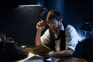 Orta keskinlikte. Masada oturmuş ne yazacağını düşünen genç bir yazarın portresini yakından çek. Onun bir elinde bir kitap, diğer elinde bir sigara var. Masanın üzerinde antika bir daktilo, bir bardak viski, bir kül tablası, kitaplar var..