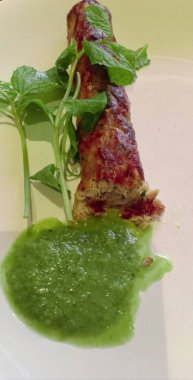 Nane yaprağıyla sebzeli börek ve beyaz arka planda yeşil turşuyla servis ediliyor.