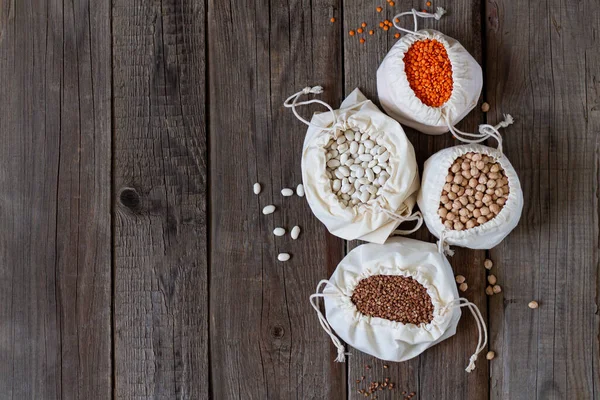 Set of gluten free grains in eco linen bags (chickpeas, lentils, beans and buckwheat). Healthy clean raw groats on rustic wooden table with copy space