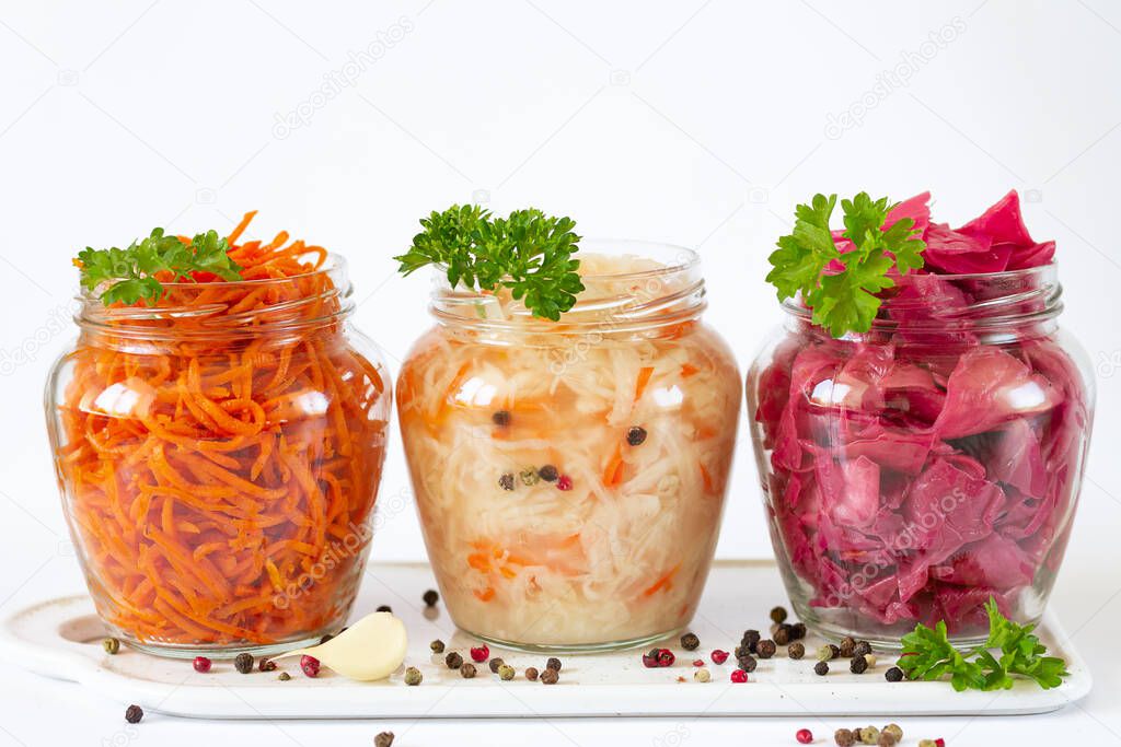 Fermented and preserved vegetarian food concept. Sauerkraut, marinated red cabbage and carrot in open glass jars on ceramic board