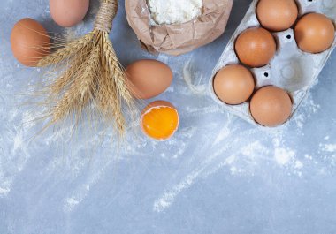 Fırın malzemeleri: yumurta, buğday kulakları ve taş masa manzaralı kağıt un torbası. Metin için boşluk