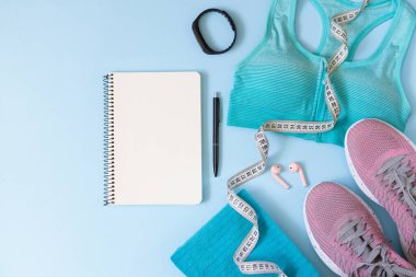 Antrenman planı konsepti. Şık kadın spor malzemeleri, giyim, alet edevat ve boş not defteri üst görünümü.