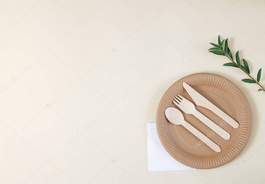 Biodegradable paper plate with cutlery, napkin and green leaves on beige background top view. Zero waste, plastic free concept. Space for your text