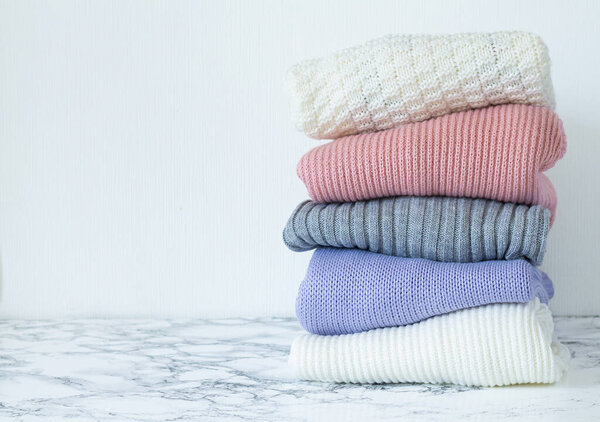 Stack of pastel color clothes. Pile of folded warm sweaters on marble table with space for your text