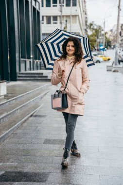 Şemsiyenin altında yakışıklı kıvırcık mestizo kadın yağmurlu bir günde Megapolis sokaklarında yürüyor.