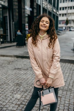 Güzel gülümseyen, şehrin sokaklarında yürüyen ve yağmurlu bir günde arkasını dönen alımlı, genç kıvırcık bir kadın.