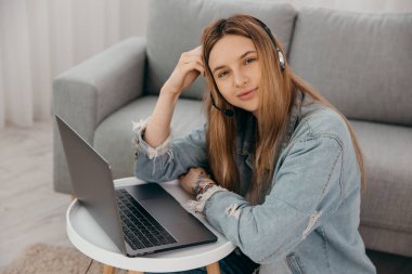 Gülümseyen genç kız kulaklık takıyor ve laptoptan arıyor. Mutlu melez kız öğrenci bilgisayar ekranına bakıyor webinar izliyor ya da webcam 'den görüntülü sohbet yapıyor..