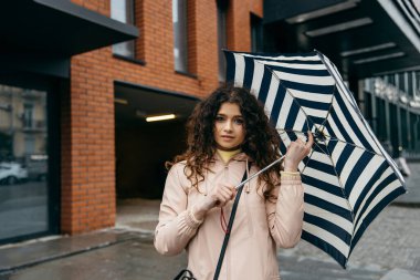 Şemsiyenin altında yakışıklı kıvırcık mestizo kadın yağmurlu bir günde Megapolis sokaklarında yürüyor.