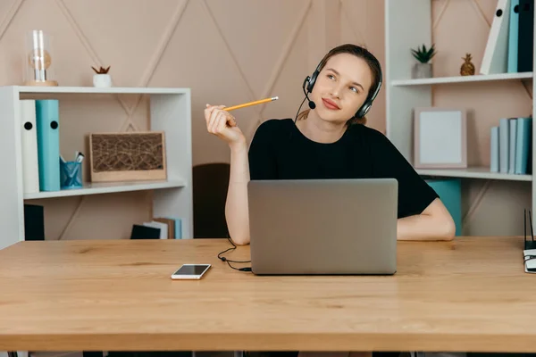 Gülümseyen mutlu kulaklıklı iş kadını masaya oturur, dizüstü bilgisayara bakar, notlar alır, kişisel gelişim webinarına katılır, internette eğlenir, video aracılığıyla iletişim kurar.