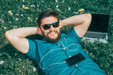 Onun dizüstü bilgisayarın yakınında çim üzerinde yalan yorgun serbest meslek. Ellerini başının arkasında ile dinlenme güneş gözlüğü yakışıklı adam